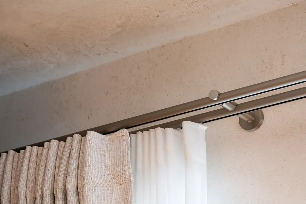 A double brushed-steel pole on a bracket, carrying a linen curtain in pleats and a white sheer
