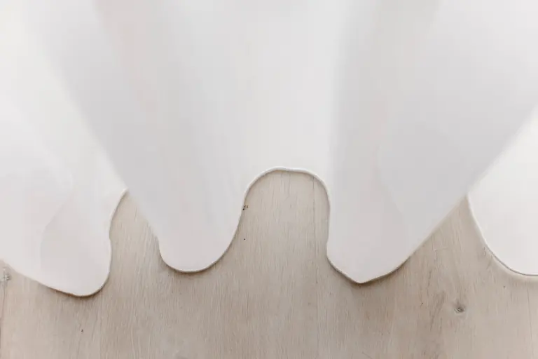 The hem of a sheer in wave folds, just touching a pale oak floor.