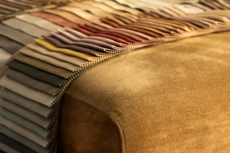 A fan of fabric swatches draped over a velvet ottoman in warm light