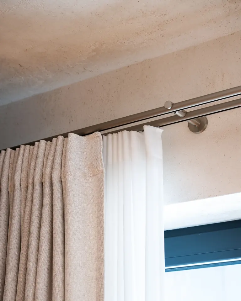 A double brushed-steel pole with a bracket, a linen curtain in folds and a white sheer