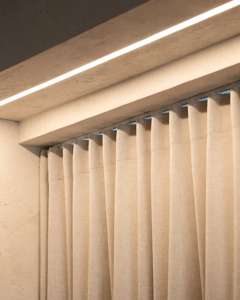 A plastered ceiling recess with a light strip, with a track hidden in it and a linen curtain in wave folds