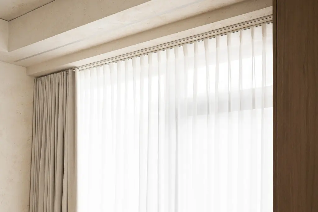 Window recess. A white sheer in wave folds and a pale side curtain on a ceiling track in a ceiling recess.