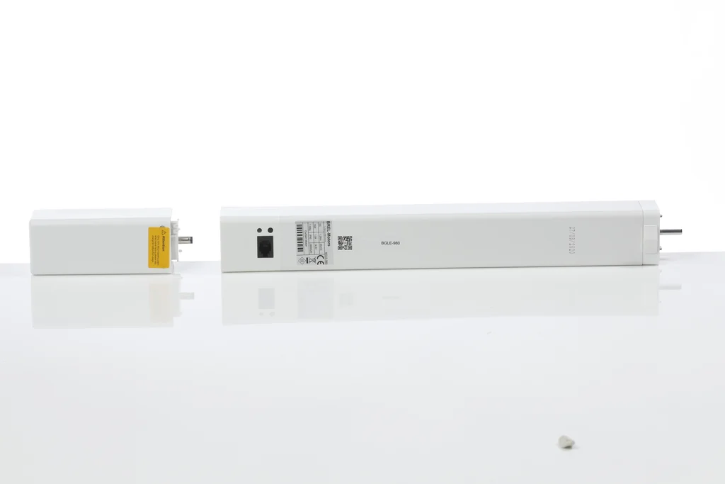 Brel Home BGLE-980 battery curtain-track motor: a long white motor housing and, beside it, a separate shorter white unit with a yellow warning label